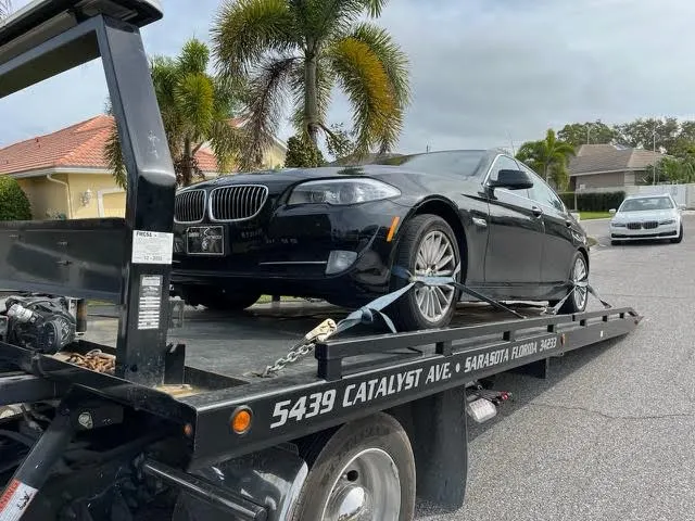 Black sedan strapped to an Action Towing flatbed whose deck reads 5439 Catalyst Ave, Sarasota Florida 34233