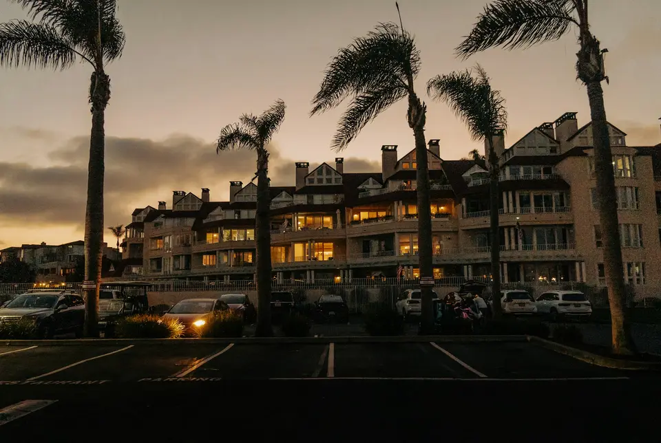 Palm trees silhouetted over a parking lot in front of a lit condominium building at dusk
